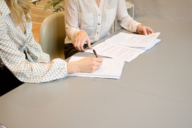 woman sighing on white paper printer beside woman about to touch the documents